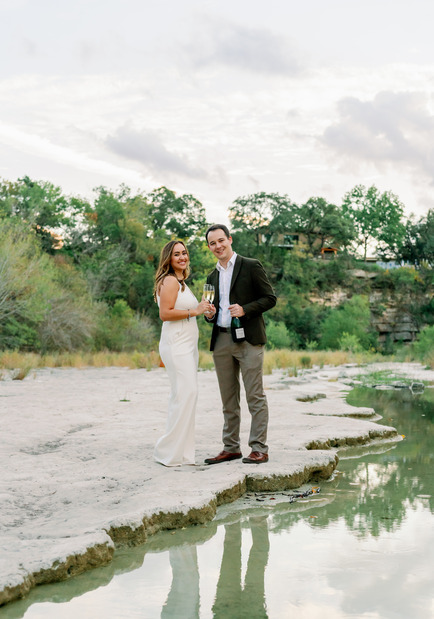 Engagement photo session of a couple standing by the water with champagne
