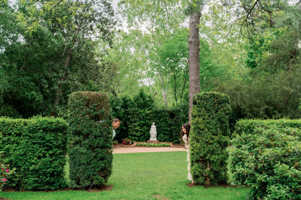Engaged couple peeks out from hedges at Bayou Bend Collection in Houston, Texas
